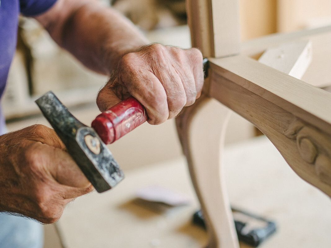 A man uses a hammer and chisel to carve a wooden chair.