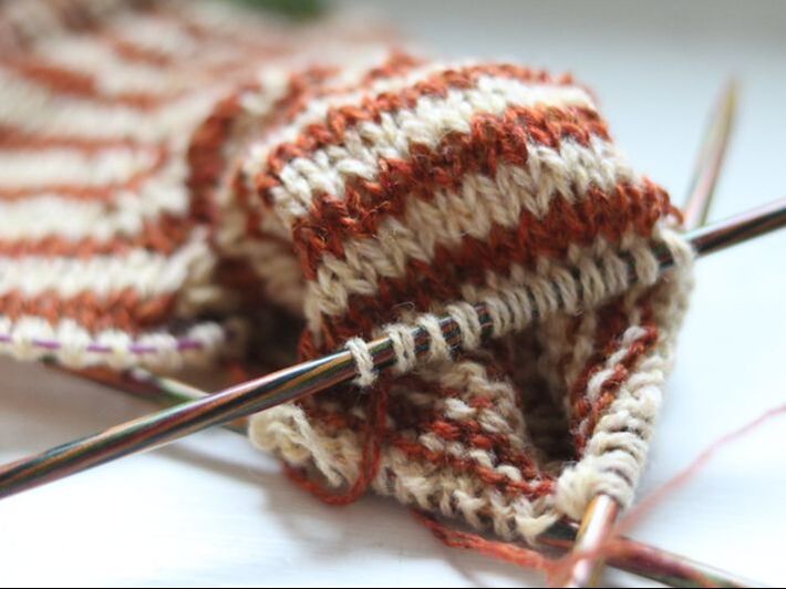 Red and white striped yarn being knit on three needles.
